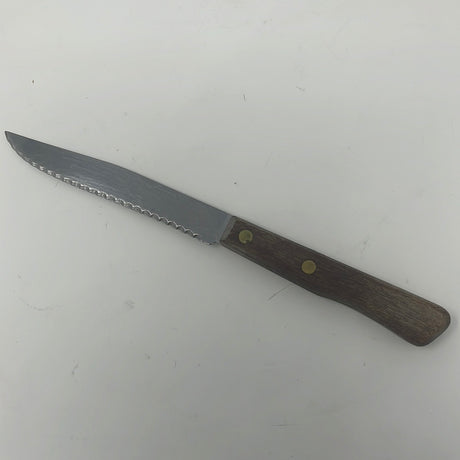 Forgecraft serrated knife with wooden handle, ideal for tomatoes. Close-up of the blade on a white surface, with a coin placed on the handle.