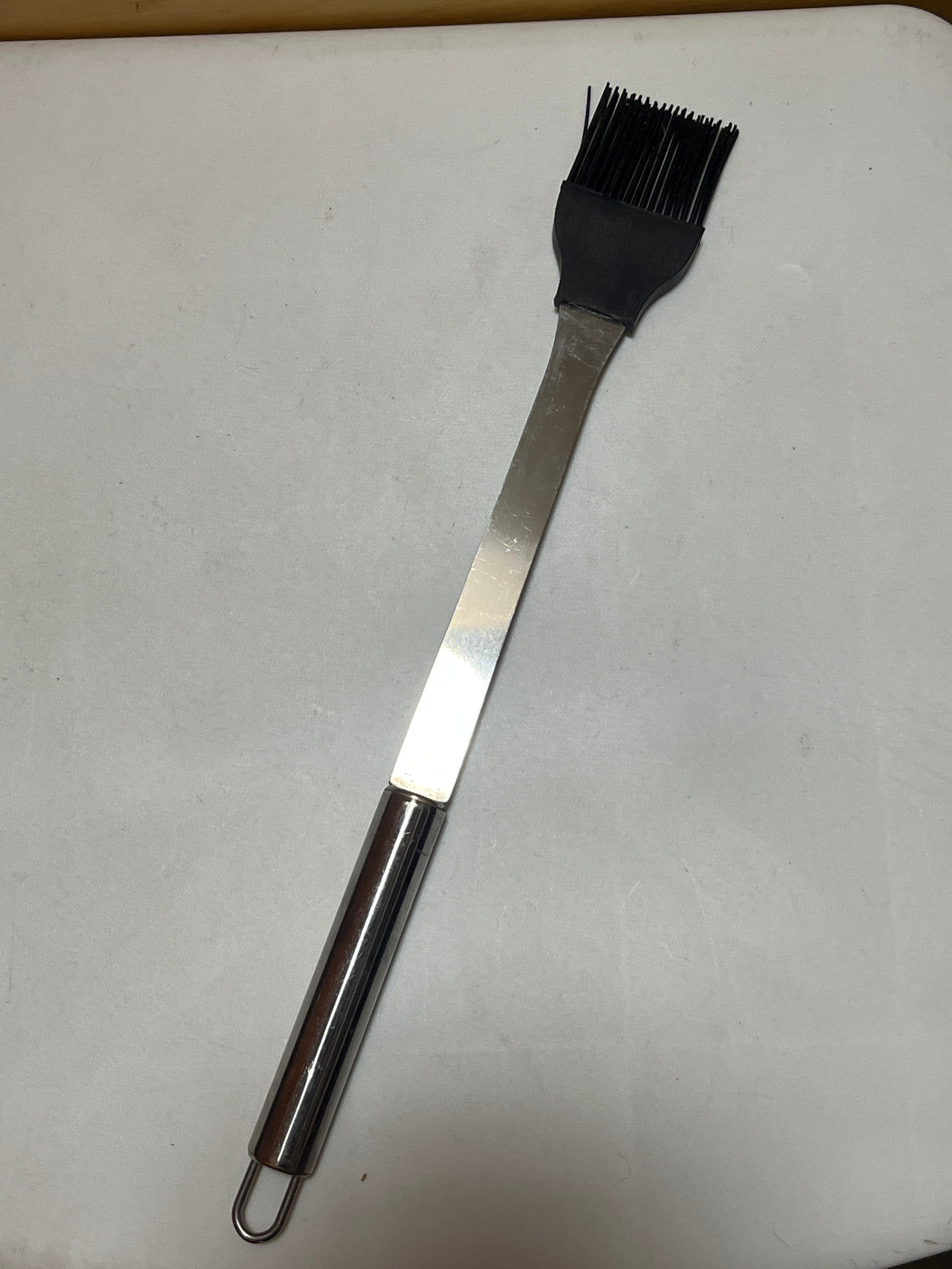 Silicone basting brush with metal handle featuring heat-resistant bristles, ideal for grilling. Long handle keeps hands safe from heat while basting.
