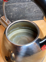 Interior view of Whistling tea kettle - Farberware 2.5 quart - black handle with red accents, showing mineral build-up inside the stainless steel.