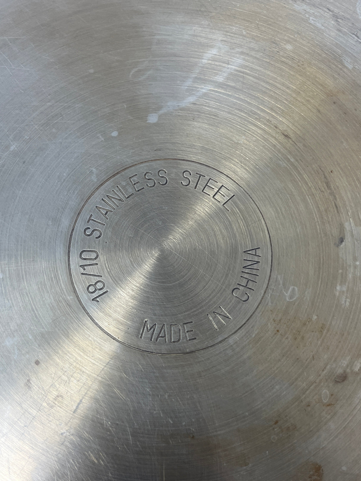 Circular stainless steel sauté pan with glass lid, featuring close-up of engraved numbers and text on metal surface, ideal for single servings.