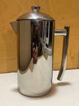 Frieling stainless steel French press coffee maker with a polished cylindrical body, spout, handle, and knob-topped lid, displayed on a simple surface.
