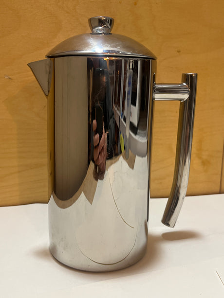 Frieling stainless steel French press coffee maker with a polished cylindrical body, spout, handle, and knob-topped lid, displayed on a simple surface.