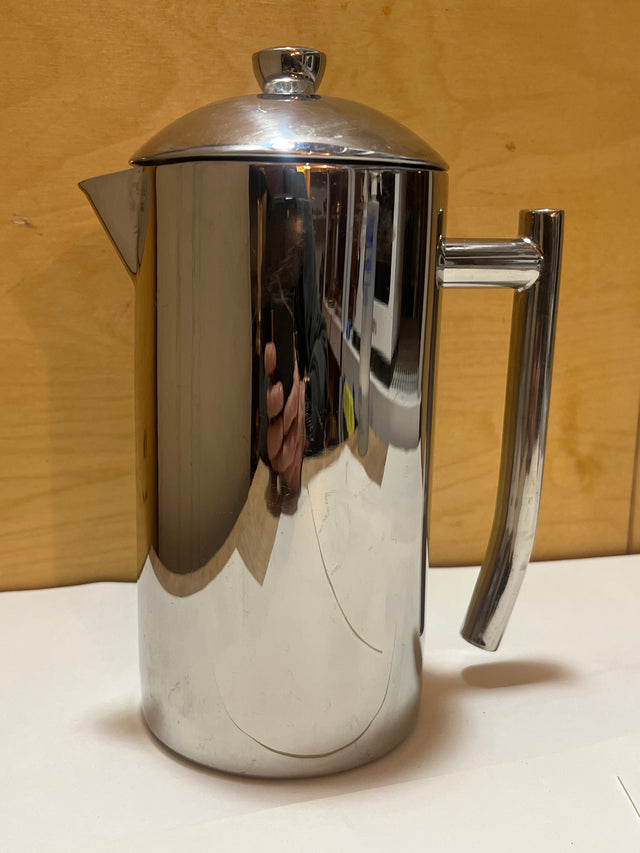 Frieling stainless steel French press coffee maker with a polished cylindrical body, spout, handle, and knob-topped lid, displayed on a simple surface.