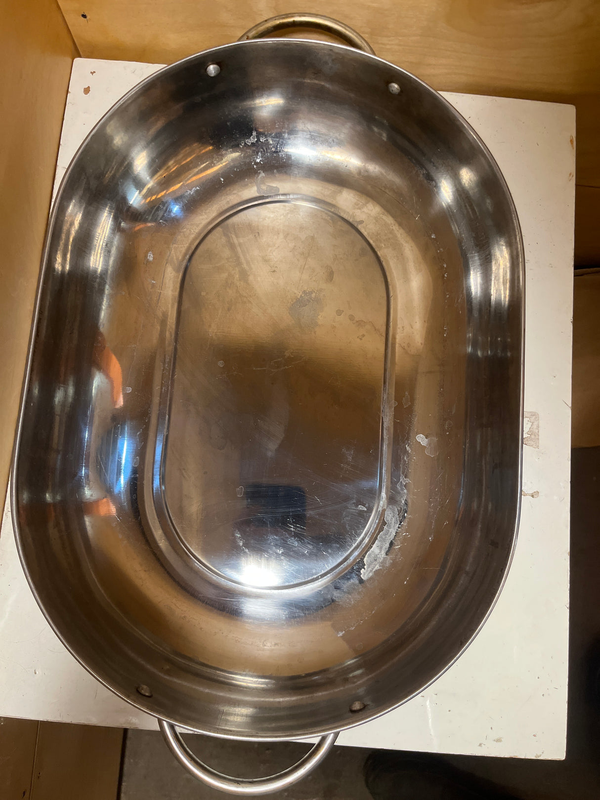 Stainless steel oval roasting pan with rack and lid, featuring two loop handles on a white surface, showcasing its spacious, durable design for versatile cooking.