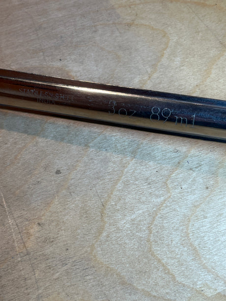 Stainless steel ladle with white handle, marked 3 oz 89 ml, rests on wood, ideal for soups and dressings with a secure grip.