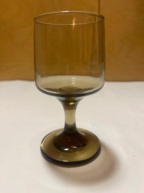 Libbey Tawney wine glass, a single amber-tinted goblet with a stem, displayed on a white surface, set against a warm wooden backdrop.