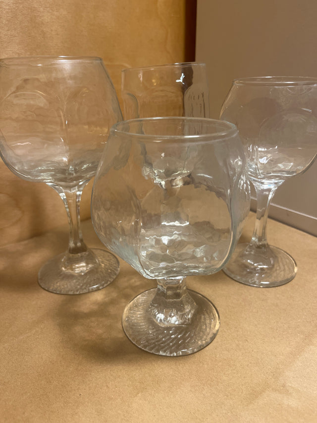 Libbey Chivalry glassware featuring four clear, hammered-texture, stemmed goblets, designed in a snifter style, perfectly displayed on a flat surface.