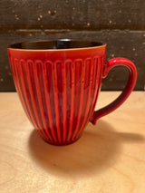 Mug - ribbed ceramic red glad exterior black interior, featuring a smoothly curved handle and vertical ribbing, displayed on a light wood surface.