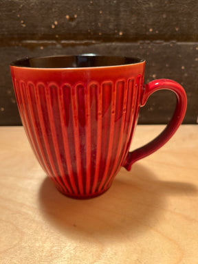 Mug - ribbed ceramic red glad exterior black interior, featuring a smoothly curved handle and vertical ribbing, displayed on a light wood surface.