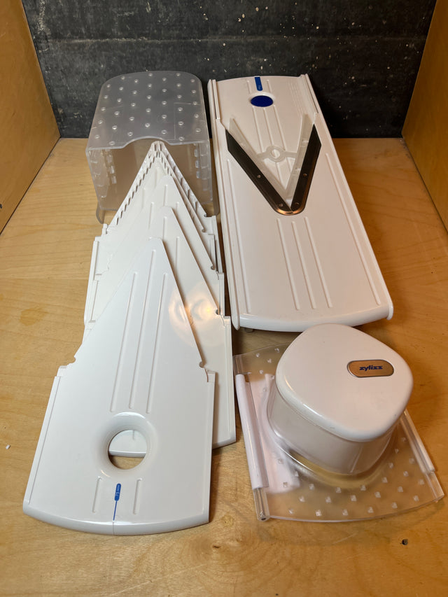 Zyliss Easy Slice mandolin, featuring a V-shaped stainless blade, interchangeable thickness inserts, a clear base tray, and a food pusher for safe slicing.