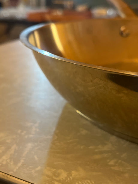 10-Inch stainless steel frying pan with a shiny, slightly golden interior and flared sides for easy cooking, featuring a riveted handle for a firm grip.