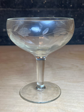 Princess House Heritage Pattern etched glass wine goblet with a shallow, rounded bowl and delicate floral-and-leaf etching, displayed on a light wood surface.
