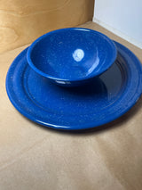 Blue speckled enamelware plate and bowl nested together on a plain surface, showcasing their lightweight and durable design ideal for outdoor activities.