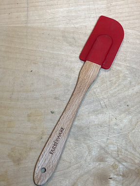 Silicone spatula - red Farberware with wood handle, featuring a flexible silicone blade and branded wooden handle, resting on a wooden surface. Heat-resistant design.