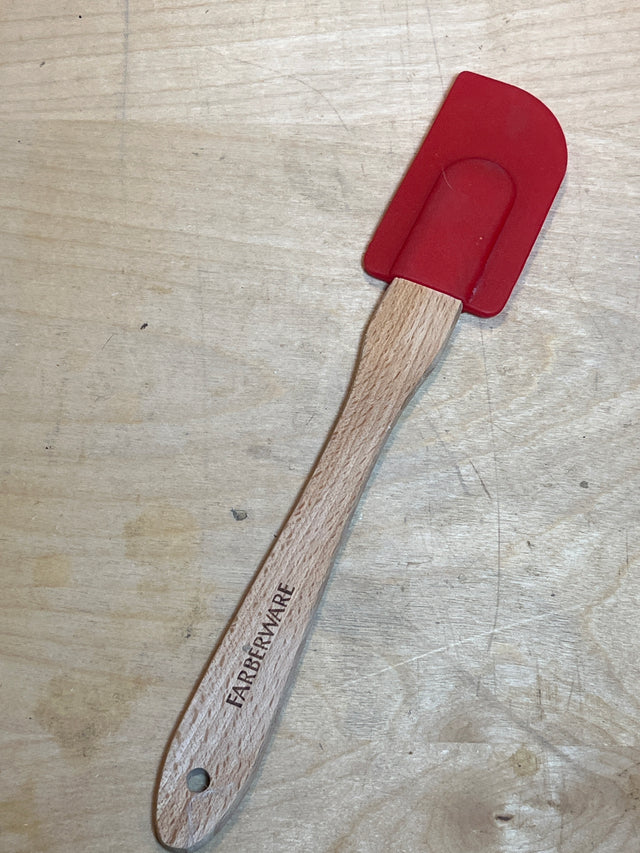Silicone spatula - red Farberware with wood handle, featuring a flexible silicone blade and branded wooden handle, resting on a wooden surface. Heat-resistant design.