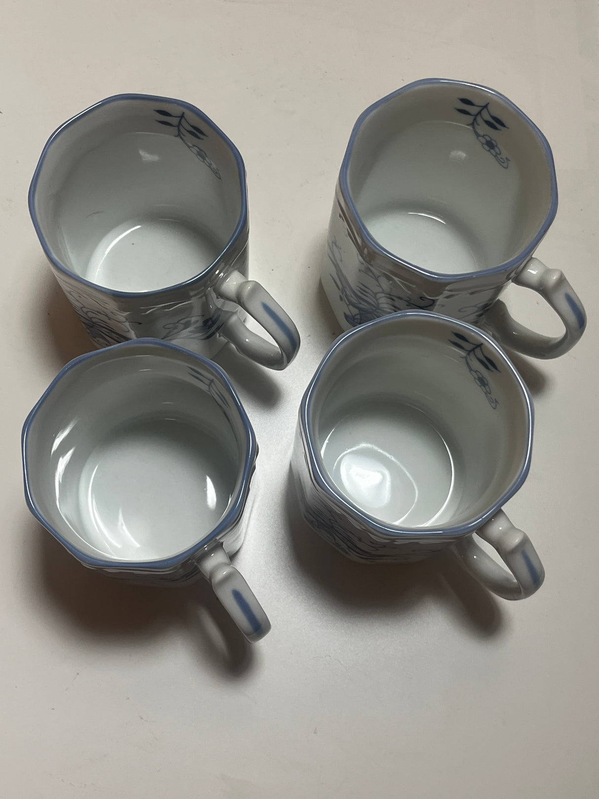 Set of 4 Arnhart Blue Onion coffee mugs with ornate handles, embossed floral rims, and slightly angular sides, in glossy white ceramic with blue illustrations.