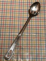 Extra long slotted basting spoon - JR stainless steel, featuring a durable, easy-to-clean long handle, resting on a tabletop with a grid-patterned tablecloth.