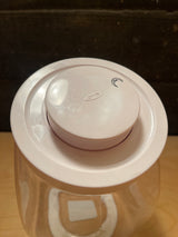 Top view of an empty OXO POP medium food storage jar 3 qt. with a white push-button lid, embossed logo visible, set in a clear canister.