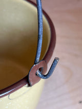 Mini pot with lid and wire handle - vintage enamelware in yellow, showcasing a close-up of its bent metal handle attached to a stamped bracket.
