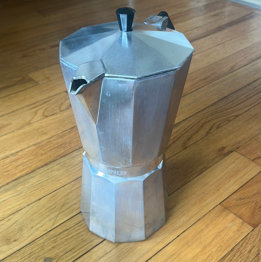 A large 12-cup Primula espresso moka pot on a wood floor. Minor stains from normal use. Ideal for study sessions or brunch.