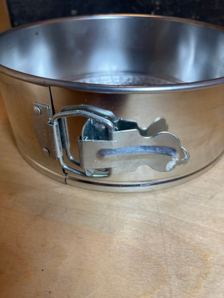 Close-up of the latch mechanism on the Springform cake pan - light tin, 8” diameter, highlighting its removable bottom and adjustable sides for easy cake release.
