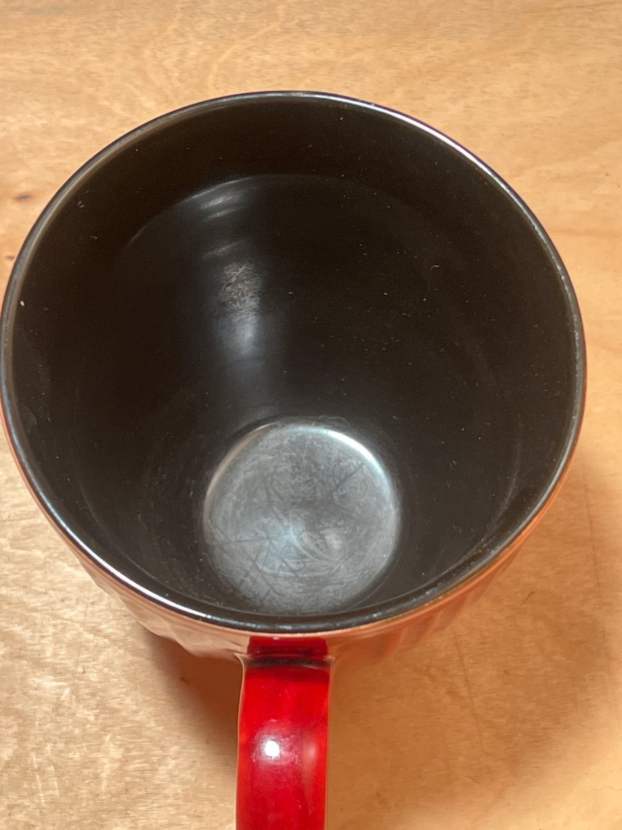 Ribbed ceramic mug with deep red glaze, red handle, and black interior, sitting empty on a wooden surface.