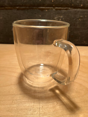 Double-walled insulated glass mug - BTäT, featuring a clear, double-walled design with a molded handle, resting on a light wood surface.