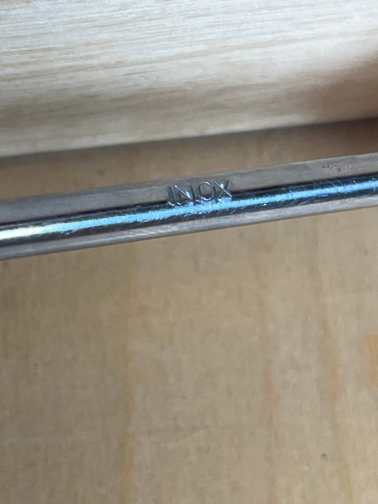 Close-up of Pedrini stainless steel slotted serving spoon, showcasing the “INOX” stamp, resting on a wooden surface, highlighting its durable stainless steel construction.