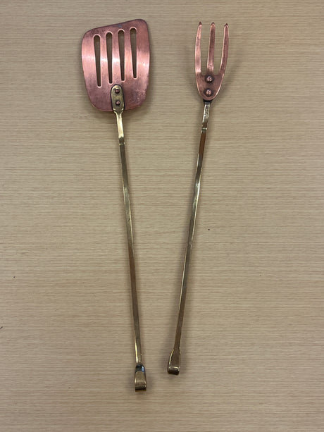 Set of copper grill tools with brass handles, featuring a spatula and grill tong on a table, showing minor tarnish, designed for durability and easy storage.