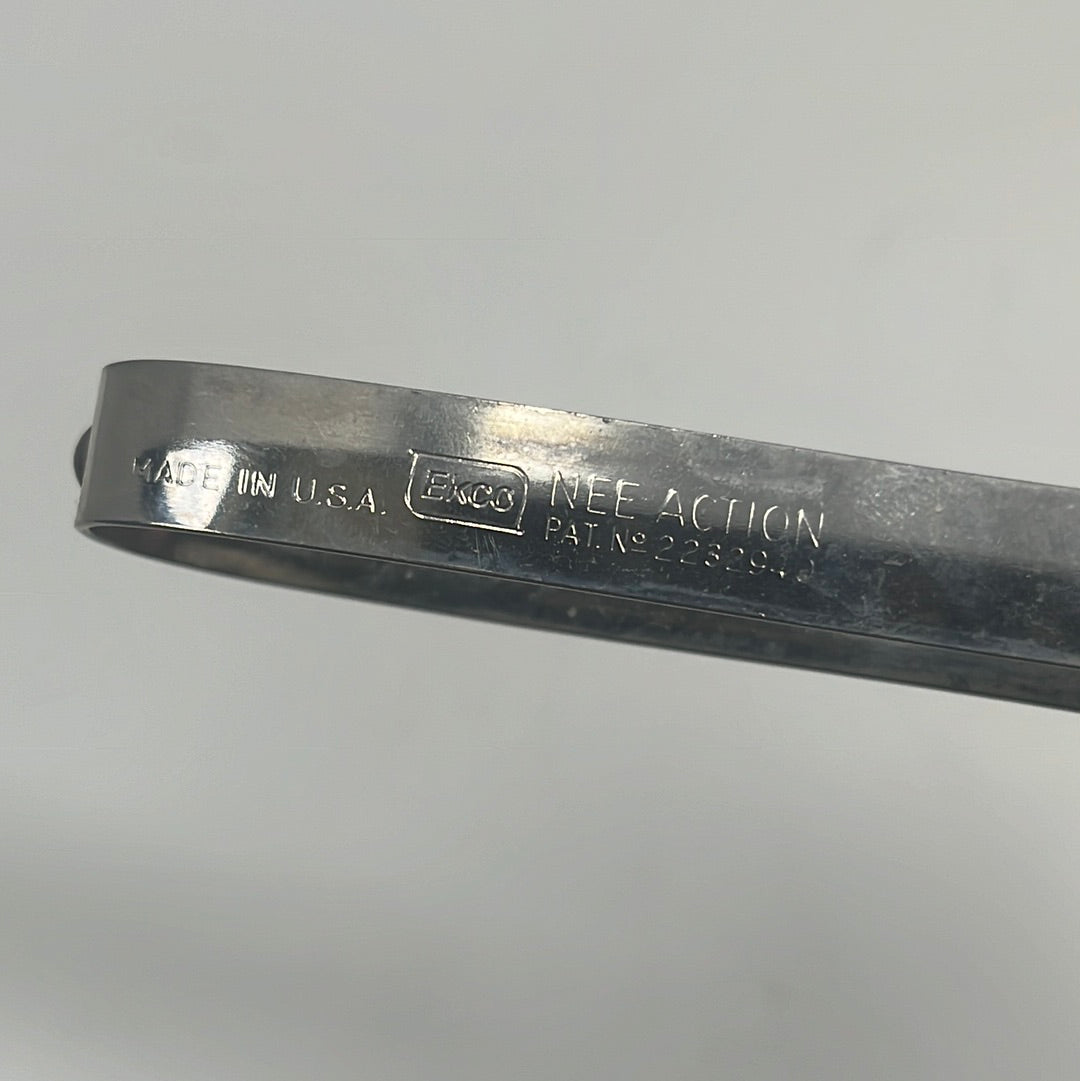 Close-up of EKCO stainless steel vegetable peeler with floating blade. Curved tip for precise cuts, inscribed with “NEE ACTION PAT. NO 2232940”.