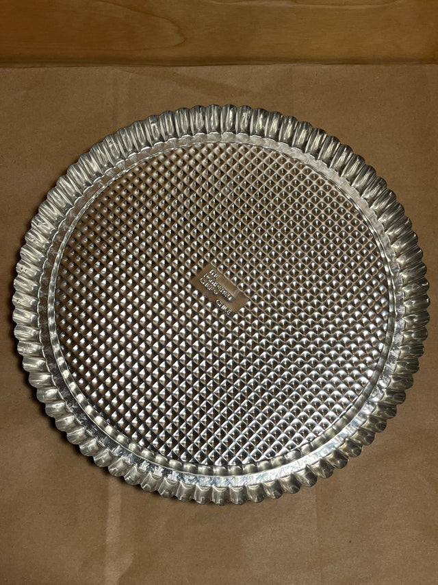 Pampered Chef stainless steel flan pan with a round, fluted edge and diamond-textured base, ideal for baking quiches and tarts with easy unmolding.