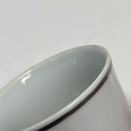 A close-up of a white ceramic ABCO espresso cup with gold trim made for United Airlines, showing slight wear on the rim.