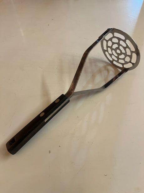 Potato masher with black handle, featuring a vintage design. Notched handle allows for easy gripping and hanging, crafted from household stainless steel for durability.