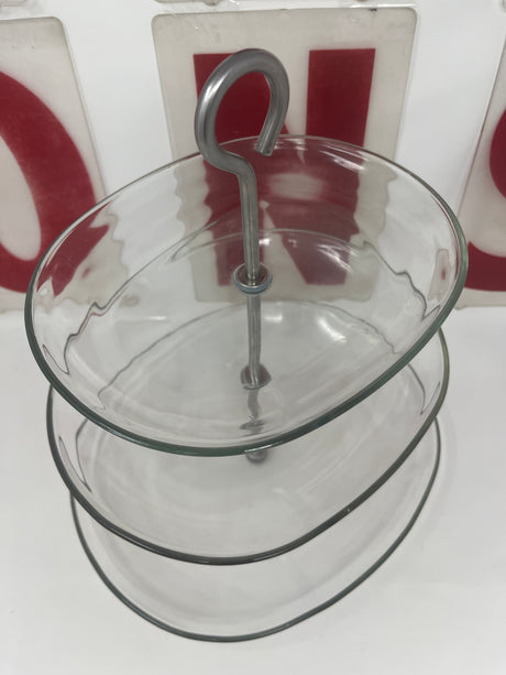 Three-tier oval glass serving stand with stainless steel base, featuring a metal handle on top, ideal for displaying appetizers, desserts, and hors d'oeuvres.