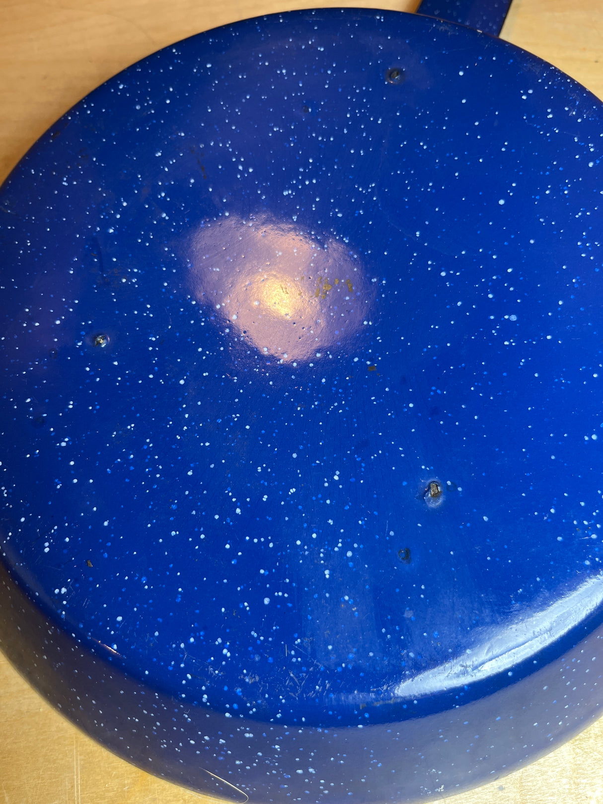 Underside of blue speckled enamelware fry pan for camping, showing minor rim damage; designed for outdoor cooking with a long handle for safety.
