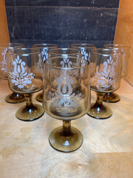 Set of 8 smokey wine glasses with etched floral motif by Pfaltzgraff, featuring vintage-style, amber-tinted glass with short stems, displayed on a wooden surface.