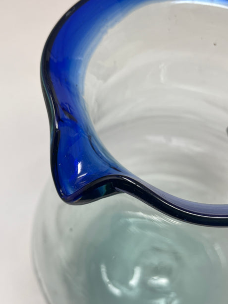 Handblown glass pitcher with blue rim and handle, featuring a wide base and handle for easy pouring, suitable for serving 4-6 people.