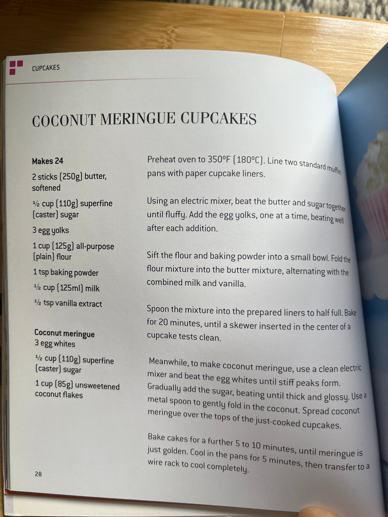 A cookbook open to a recipe for cupcakes & muffins, showcasing a close-up of a book with handwritten text and a cupcake illustration.