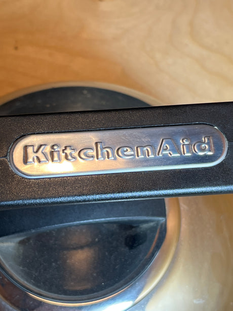 Whistling tea kettle - Kitchenaid 2 quart stainless steel with black handle, featuring a cushion grip and embossed logo, designed for easy and enjoyable tea preparation.