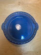 Pyrex 229 cobalt blue glass pie/casserole dish, round and translucent with fluted edges, small handles, and deep sides, shown upside-down on a wood tabletop.
