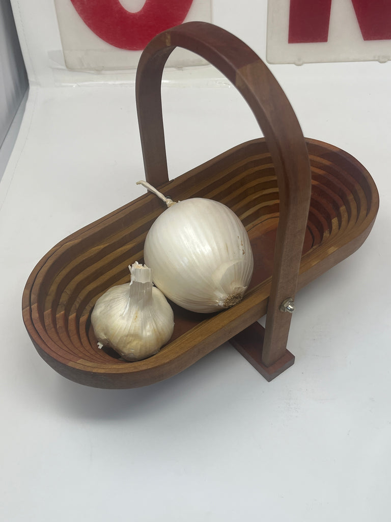 Hand-carved wood fold-a-bowl containing onions and garlic, showcasing intricate design with signed craftsmanship by C.F. Evans, featuring screw-hinged handles.