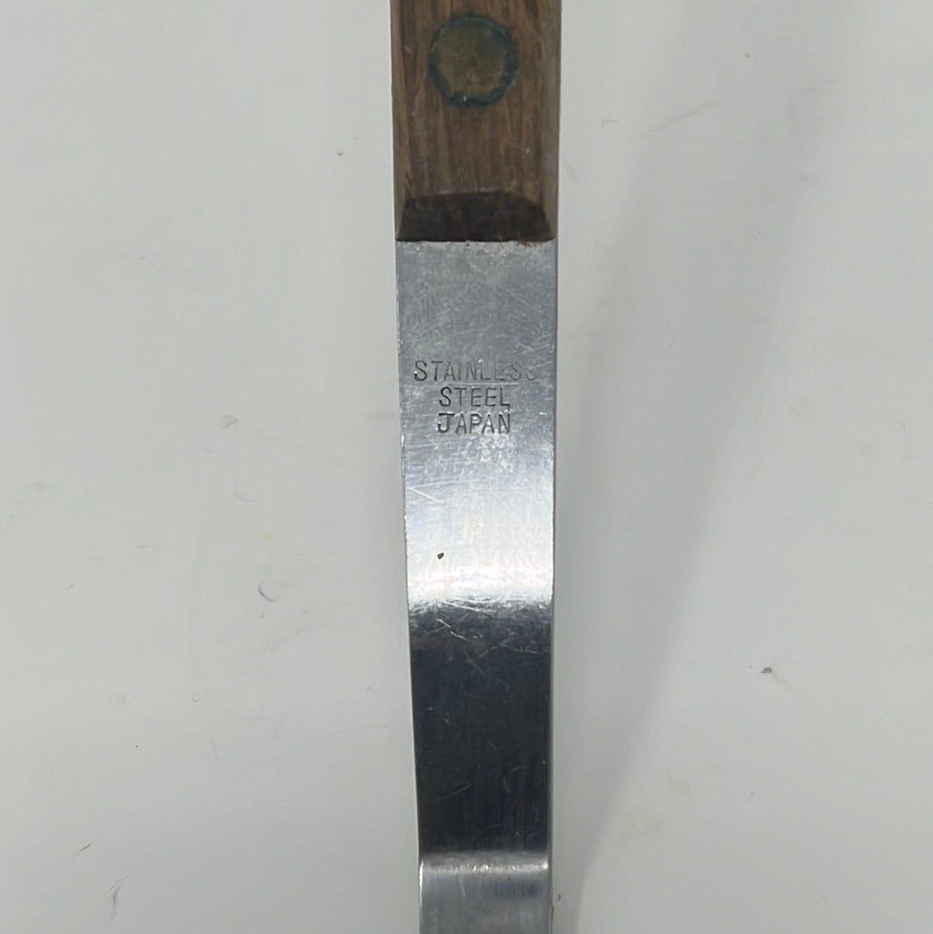 Oval slotted spatula with metal blade and wooden handle on white surface. Closeup view of the handle that says "stainless steel Japan." From Spoons Kitchen Exchange.