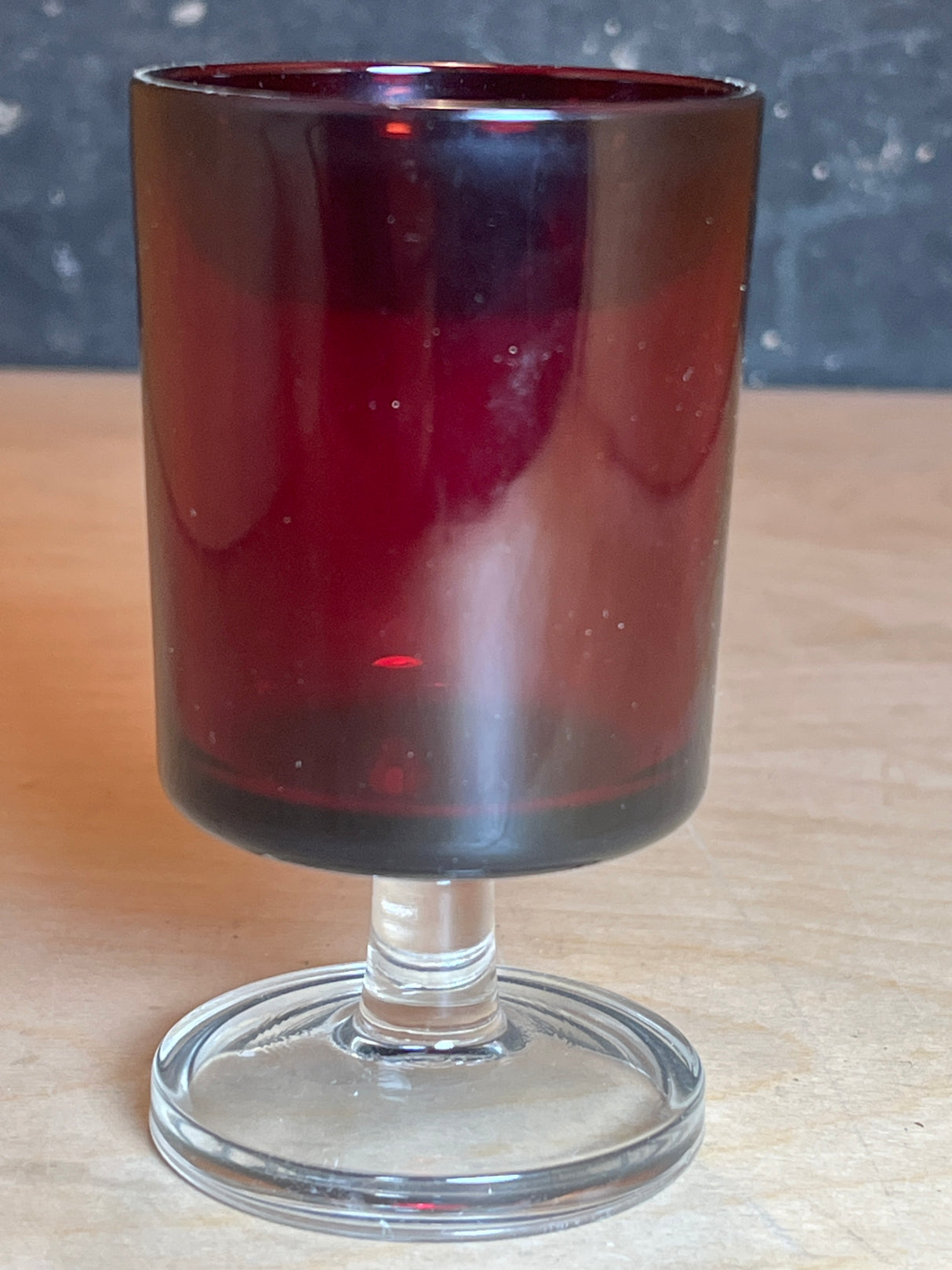 Luminarc/ARCOROC ruby red small wine glass with a deep red bowl and clear stem, displayed on a light-wood surface.