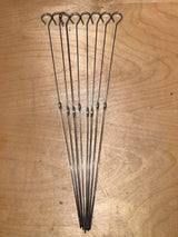 Food skewers - set of 8 reusable 14” stainless steel, featuring looped handles and pointed tips, laid out on wood, ideal for grilling or broiling.