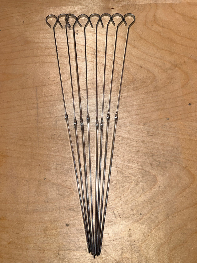 Food skewers - set of 8 reusable 14” stainless steel, featuring looped handles and pointed tips, laid out on wood, ideal for grilling or broiling.