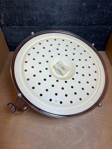 Spinner: A plastic, bowl-shaped housing featuring a removable round perforated insert with a central latch, designed for use as a filter basket in centrifugal juicers.