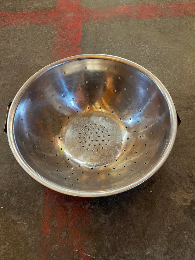 Colander with flat base: A round, lightweight stainless steel strainer, features small drainage holes and thin metal handles that may bend, ideal for rinsing greens.