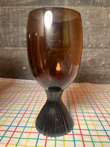 Set of 5 brown glass water goblets - vintage Lenox Nutmeg line, featuring a fluted dark stem and amber-tinted bowl on a grid-patterned tablecloth.