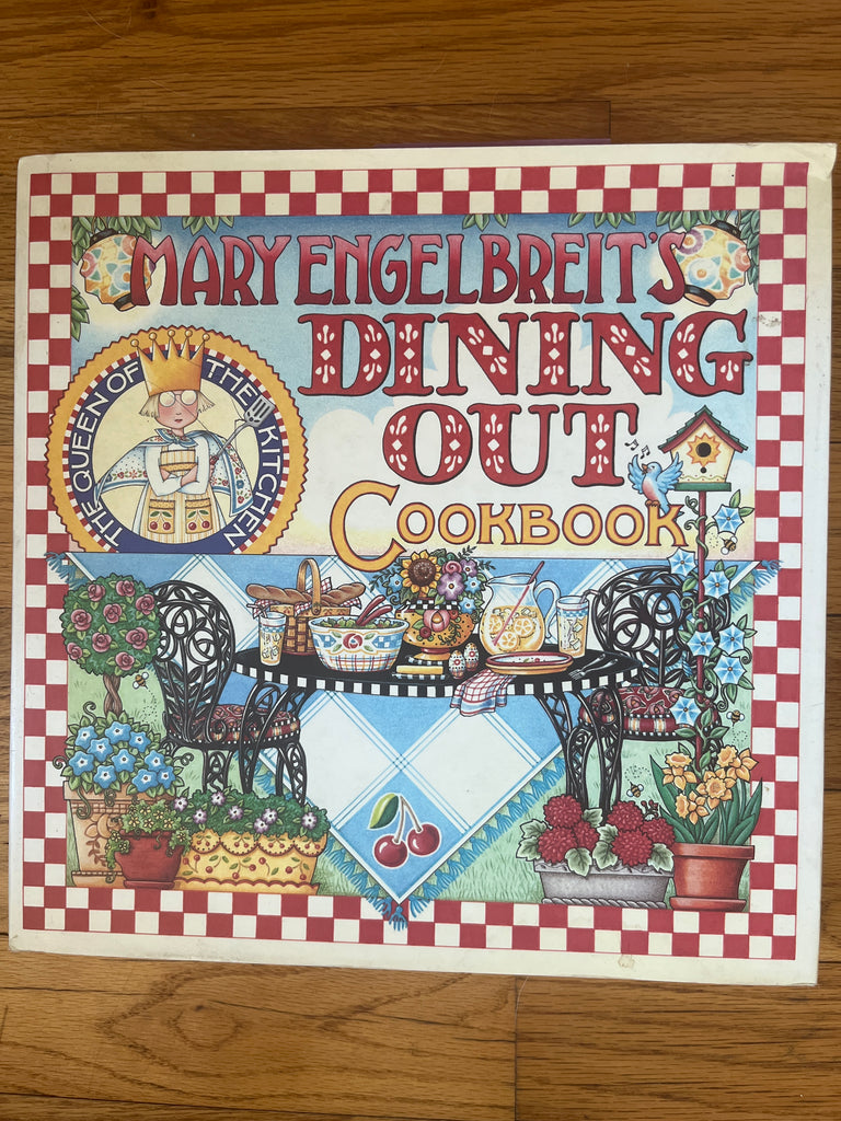 Mary Engelbreit's Dining Out Cookbook cover featuring a table with a cookbook, a cartoon woman holding a spatula, and various food items.