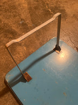 Close-up of the Vintage Metal Lap Serving Tray Game by Pressman Toy Co., featuring a U-shaped handle on a flat metal surface with rusted brackets.